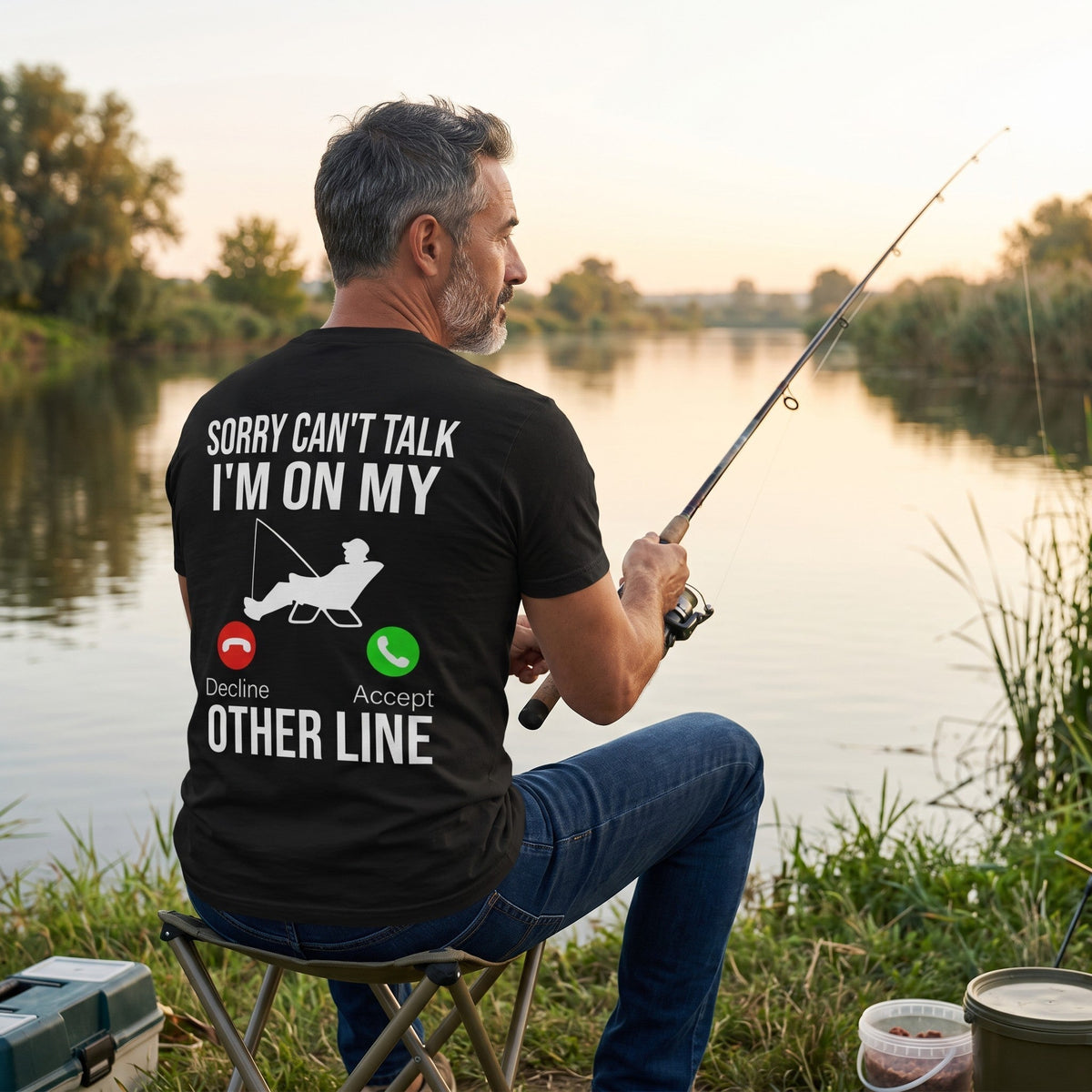 TrendyShift.Com black cotton t-shirt with Sorry Can't Talk I'm On My Other Line fishing graphic worn by a man fishing