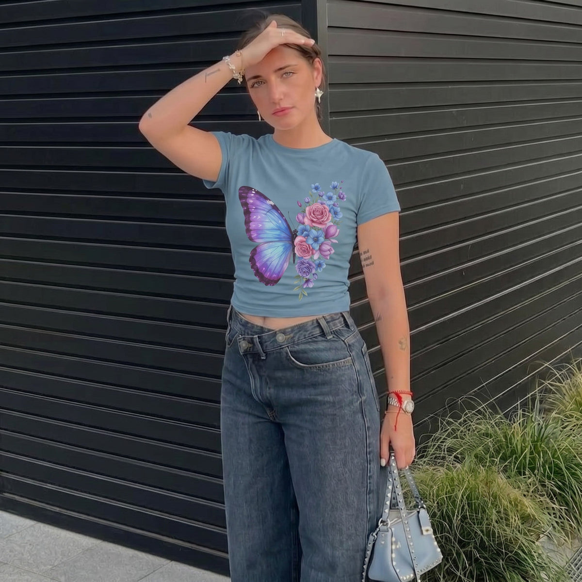 TrendyShift.Com women's blue micro rib baby tee featuring a pastel butterfly and floral print, worn with dark jeans.