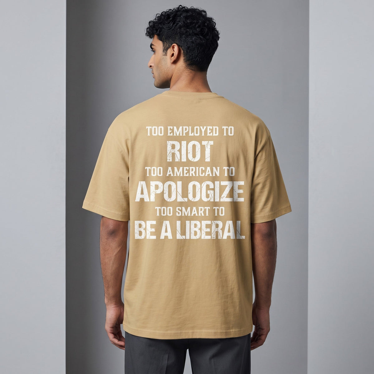 TrendyShift.Com tan oversized t-shirt with white distressed text print on the back, worn by a man from behind.